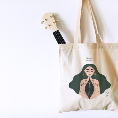 Saco de pano com ilustração de mulher e texto, com guitarra dentro, pendurado na parede