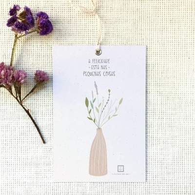 Cartão branco com vaso ilustrado e texto, flores secas ao lado sobre tecido bege