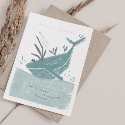 Cartão postal com ilustração de baleia azul e texto em português sobre envelope castanho e rama seca