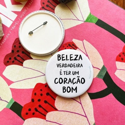 Dois bottons redondos com alfinete, um com texto em português, sobre estampa floral colorida