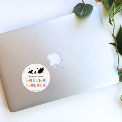 Portátil prateado com autocolante colorido e planta verde ao lado.