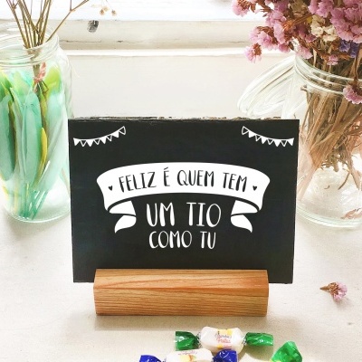 Cartão preto com texto branco em suporte de madeira, flores secas em jarros de vidro e caramelos coloridos sobre mesa branca