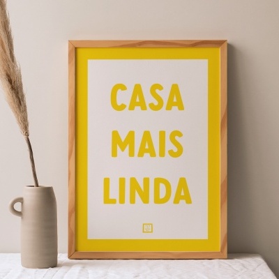 Pôster decorativo com moldura de madeira e texto amarelo ao lado de vaso cinzento com ramo seco