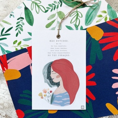 Duas caixas para presente com padrão floral colorido e cartão ilustrado com texto em português pendurado.