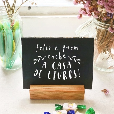 Placa preta com texto branco sobre suporte de madeira e dois jarros com ramos secos