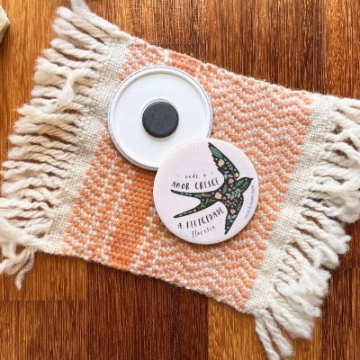 Vela branca numa base cerâmica com tampa decorada, sobre manta laranja com franjas e pedras numa superfície de madeira