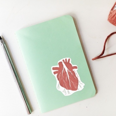 Caderno verde com autocolante de coração, caneta, novelo de fio e pássaro decorativo