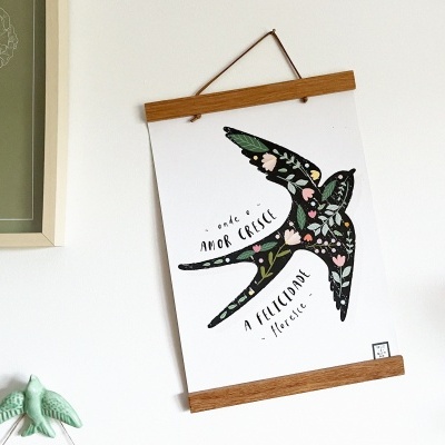 Poster com desenho de andorinha preta decorada com flores e texto em português pendurado numa parede branca