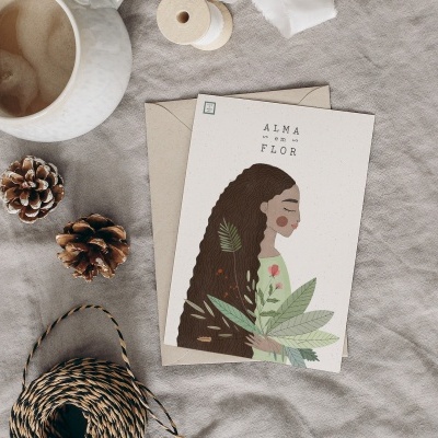 Cartão ilustrado com mulher e folhas, envelope, chávena de café, pinhas e fio sobre tecido cinzento