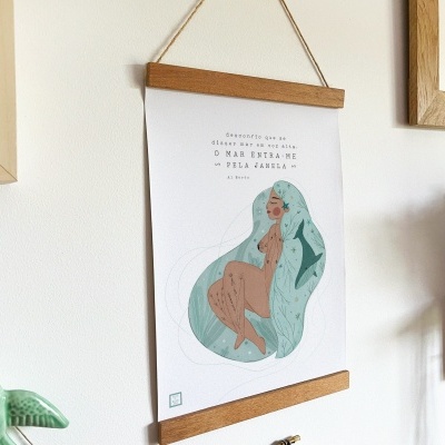 Poster decorativo com ilustração de mulher, texto e moldura de madeira pendurado numa parede branca junto a planta e prateleira.