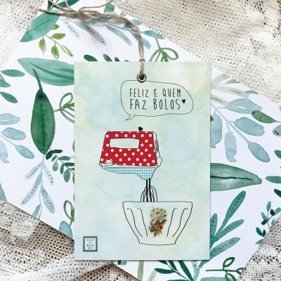 Cartão com ilustração de batedeira vermelha e taça floral e texto, sobre cadernos com padrão de folhas verdes