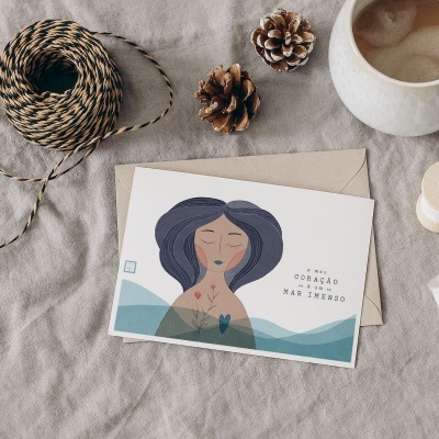 Cartão postal com ilustração de mulher, texto motivacional, caneca de café, corda, pinheiros e carretel de madeira sobre tecido cinza