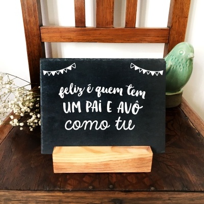 Placa preta com texto branco sobre suporte de madeira numa cadeira de madeira escura com flores e estatueta verde