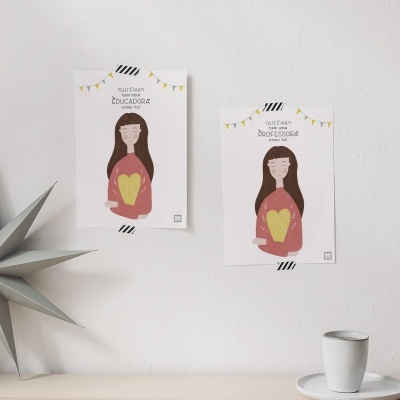 Dois posters com ilustrações de mulher e coração dourado na parede branca, estrela cinza decorativa e chávena com pires em superfície clara.