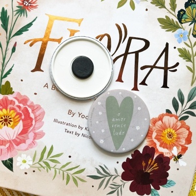 Dois botões de metal sobre livro ilustrado com flores coloridas e texto 'FLORA'