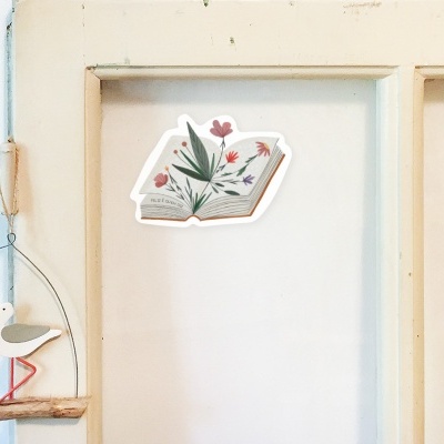 Autocolante em forma de livro aberto com flores coloridas numa porta branca e ornamento de gaivota pendurado