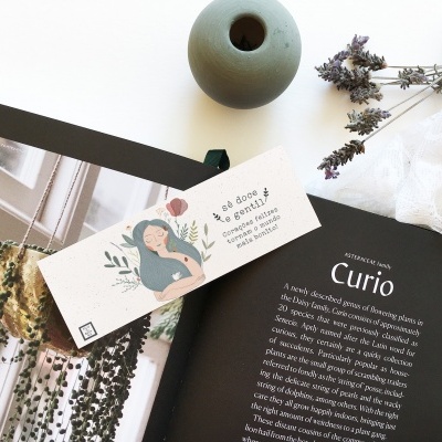 Revista aberta com artigo 'Curio', marca-páginas ilustrado, jarra cinza, lavanda seca e tecido branco sobre superfície branca