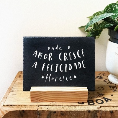 Placa decorativa preta com texto branco e vaso de planta branco em superfície de madeira