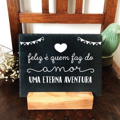 Placa decorativa preta com texto branco em suporte de madeira sobre cadeira de madeira