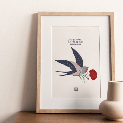 Quadro com ilustração de andorinha segurando flor vermelha sobre superfície de madeira com vasos cerâmicos ao lado