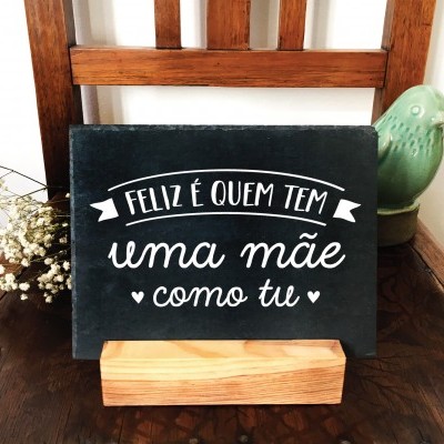 Placa decorativa preta com texto branco em suporte de madeira sobre cadeira com flores secas e pássaro verde