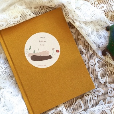 Livro com capa dourada sobre tecido branco rendado e dinossauro de madeira colorida ao lado.