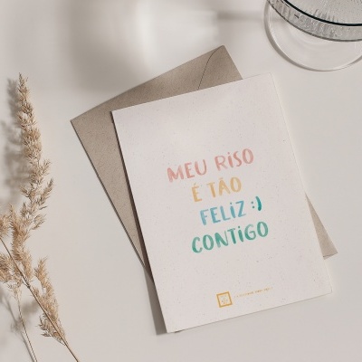 Cartão com texto colorido, envelope castanho e ramos secos sobre superfície branca