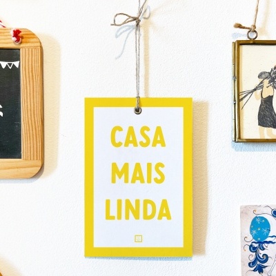 Placa decorativa amarela com texto 'CASA MAIS LINDA' pendurada na parede