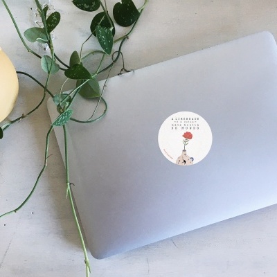 Computador portátil prata com autocolante redondo e planta verde sobre mesa clara