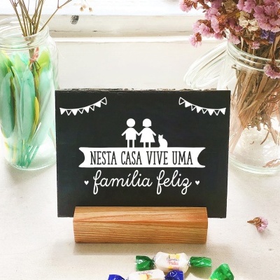 Placa decorativa preta com texto em português sobre suporte de madeira, com flores secas em frascos ao redor