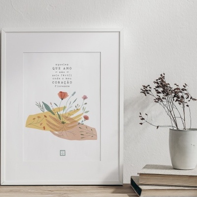 Quadro branco com ilustração de mãos e flores, texto em português, vaso branco com flores secas sobre livros