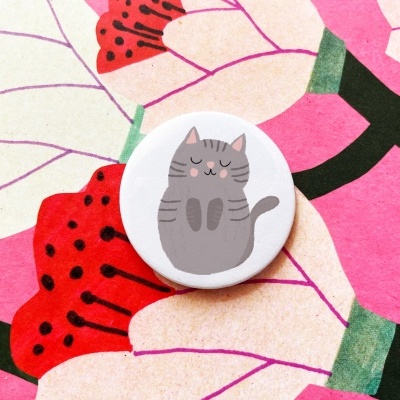 Botão branco com desenho de gato cinzento sobre padrão floral colorido