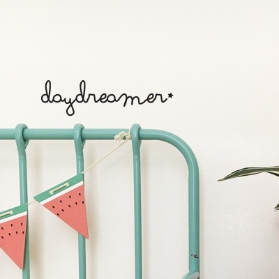 Cabeceira de cama verde água com decoração de papel em forma de melancia e texto 'daydreamer*' na parede