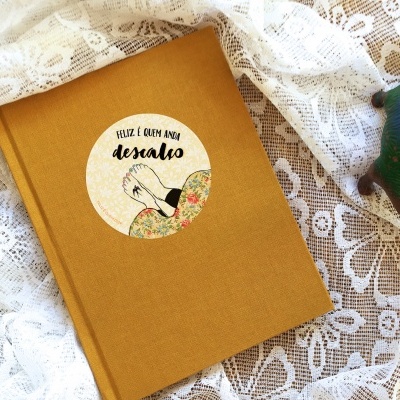 Livro castanho com autocolante redondo ilustrado e dinossauro colorido ao lado, sobre tecido rendado branco