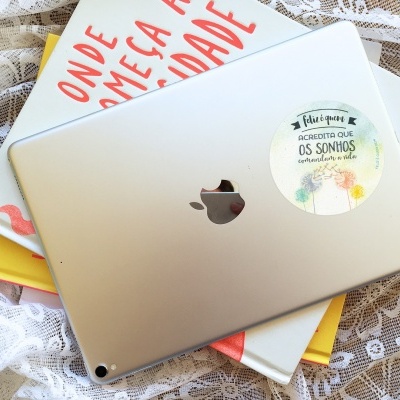 Tablet Apple prateado com autocolante redondo sobre livros em fundo de renda branca