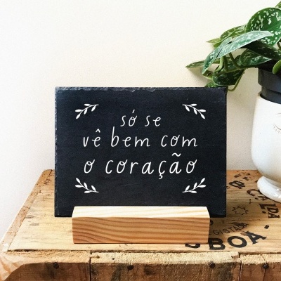 Placa preta com frase em branco ao lado de vaso com planta sobre mesa de madeira
