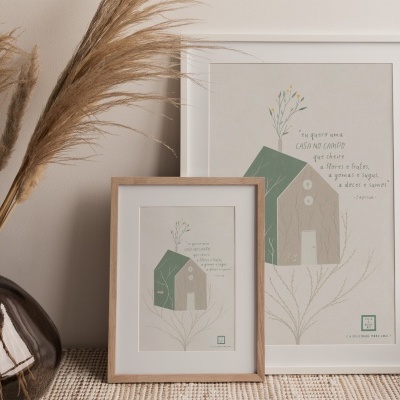 Dois quadros decorativos com ilustrações de casas verdes e texto em português junto a vaso com ramos secos