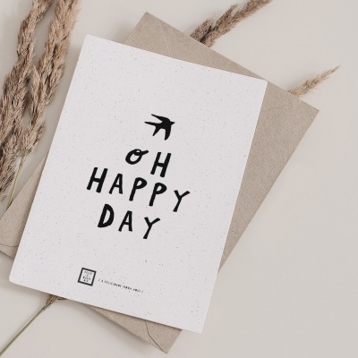 Cartão branco com texto 'OH HAPPY DAY' e envelope castanho com ramos secos ao lado