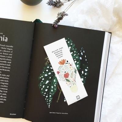 Marcador de páginas com flores e texto sobre página de livro aberto com folha verde e texto.