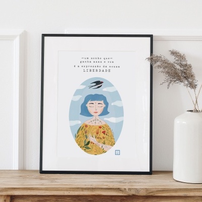 Quadro ilustrativo com mulher de cabelo azul e texto em português, em moldura preta sobre mesa de madeira junto a jarra branca com plantas secas