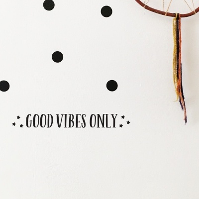 Parede branca com autocolantes de pontos pretos, frase 'GOOD VIBES ONLY' e apanhador de sonhos pendurado.