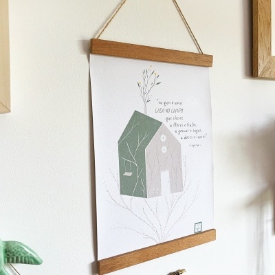 Pôster decorativo de casa verde pendurado na parede branca com moldura de madeira e prateleira com plantas