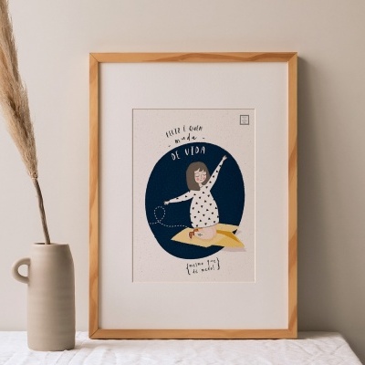 Quadro emoldurado em madeira com ilustração e texto em espanhol ao lado de vaso de cerâmica com planta seca