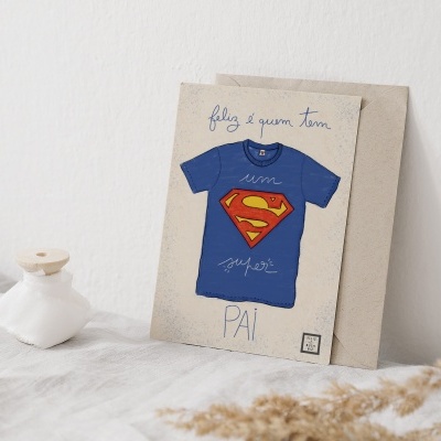Quadro decorativo com imagem de t-shirt azul com símbolo do Super-Homem e texto em português