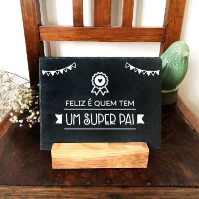 Placa decorativa preta com texto branco, base de madeira, cadeira de madeira e estatueta de pássaro verde