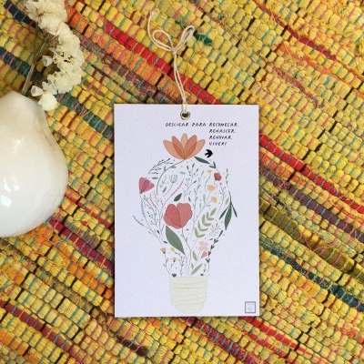 Vaso branco cerâmico sobre tapete colorido com cartão ilustrado floral.