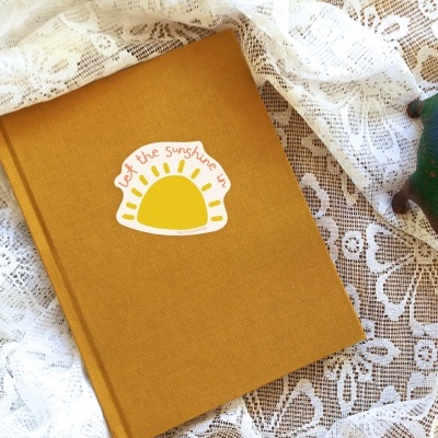 Livro amarelo com autocolante de sol sobre renda branca e figura decorativa de madeira colorida