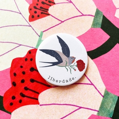 Botton branco com ilustração de andorinha e flor sobre tecido floral colorido