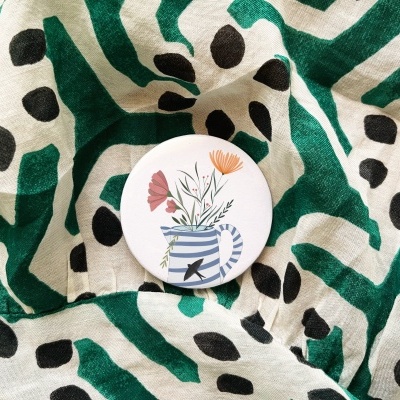 Botão redondo com desenho de vaso e flores sobre tecido estampado verde e preto