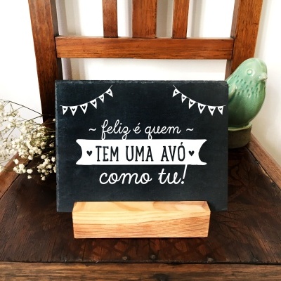 Prancha decorativa preta com texto branco sobre suporte de madeira numa cadeira de madeira escura com flores e pássaro cerâmico